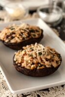 2 risotto-stuffed portobello mushrooms on a plate, garnished with a little fresh parmesan.