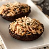 2 risotto-stuffed portobello mushrooms on a plate, garnished with a little fresh parmesan.