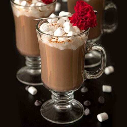 1 hot chocolate, topped with marshmallows and flower garnishes on a table, sprinkled with marshmallows and chocolate chips.