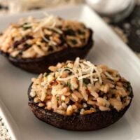 2 risotto-stuffed portobello mushrooms on a plate, garnished with a little fresh parmesan.