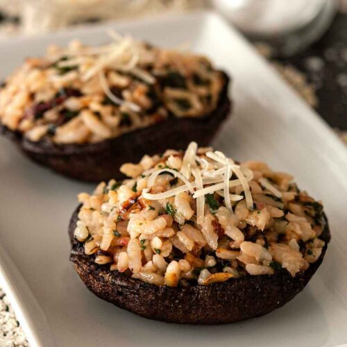 2 risotto-stuffed portobello mushrooms on a plate, garnished with a little fresh parmesan.