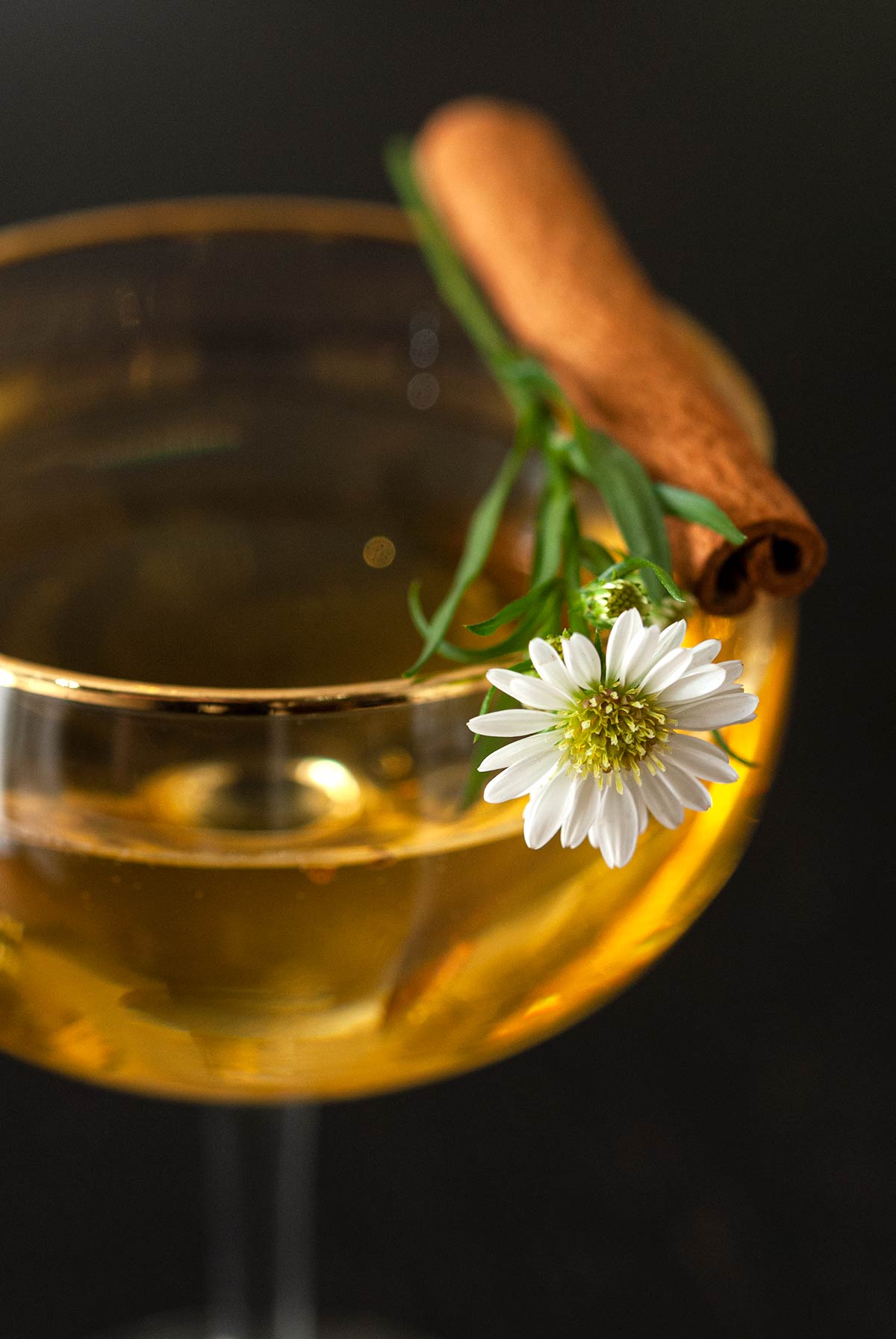 A daisy and cinnamon stick garnish on the edge of a cocktail.