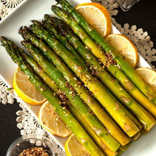 A stack of lemon asparagus on a plate, garnish with lemons.