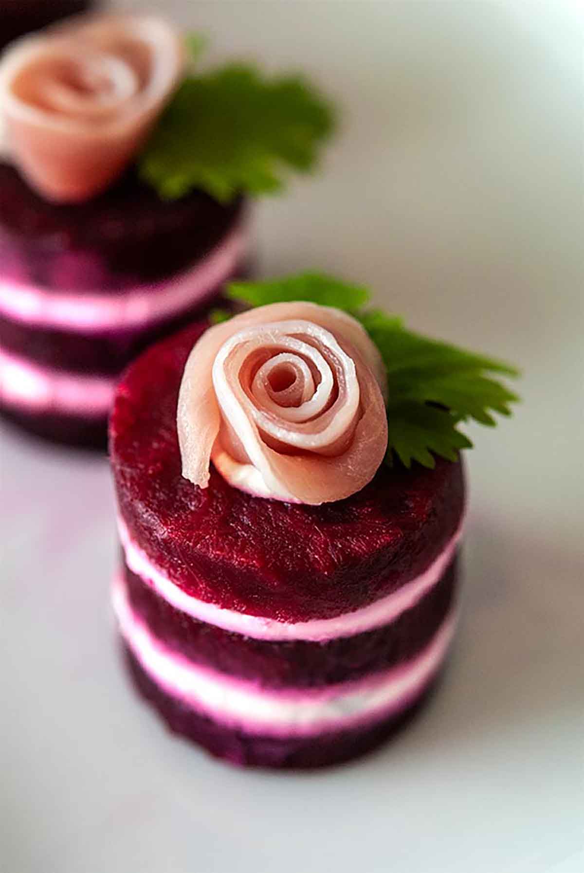 A small beet napoleon, with a prosciutto rose on top, on a white plate.