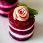 A small beet napoleon, with a prosciutto rose on top, on a white plate.