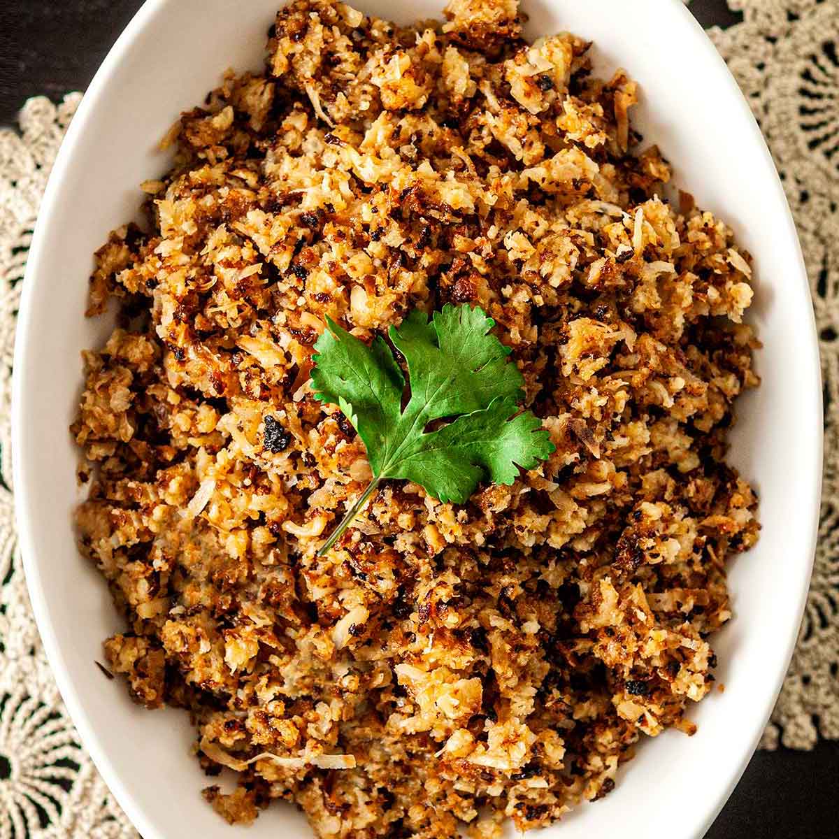 Coconut cauliflower rice in a bowl, topped with a cilantro leaf, on a table with lace.