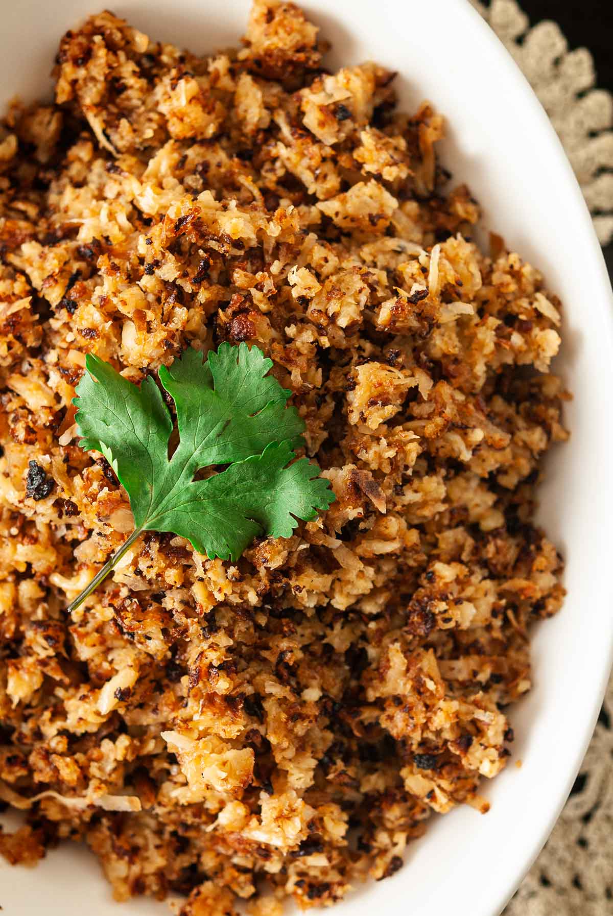 Coconut cauliflower rice in a bowl, topped with a cilantro leaf.