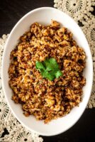 Coconut cauliflower rice in a bowl, topped with a cilantro leaf, on a table with lace.