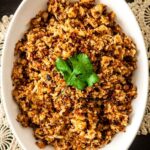 Coconut cauliflower rice in a bowl, topped with a cilantro leaf, on a table with lace.