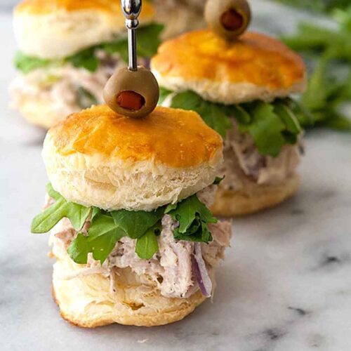 Chicken salad sliders on a marble board surrounded by arugula.