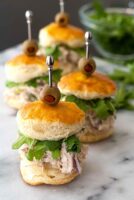 Chicken salad sliders on a marble board surrounded by arugula.