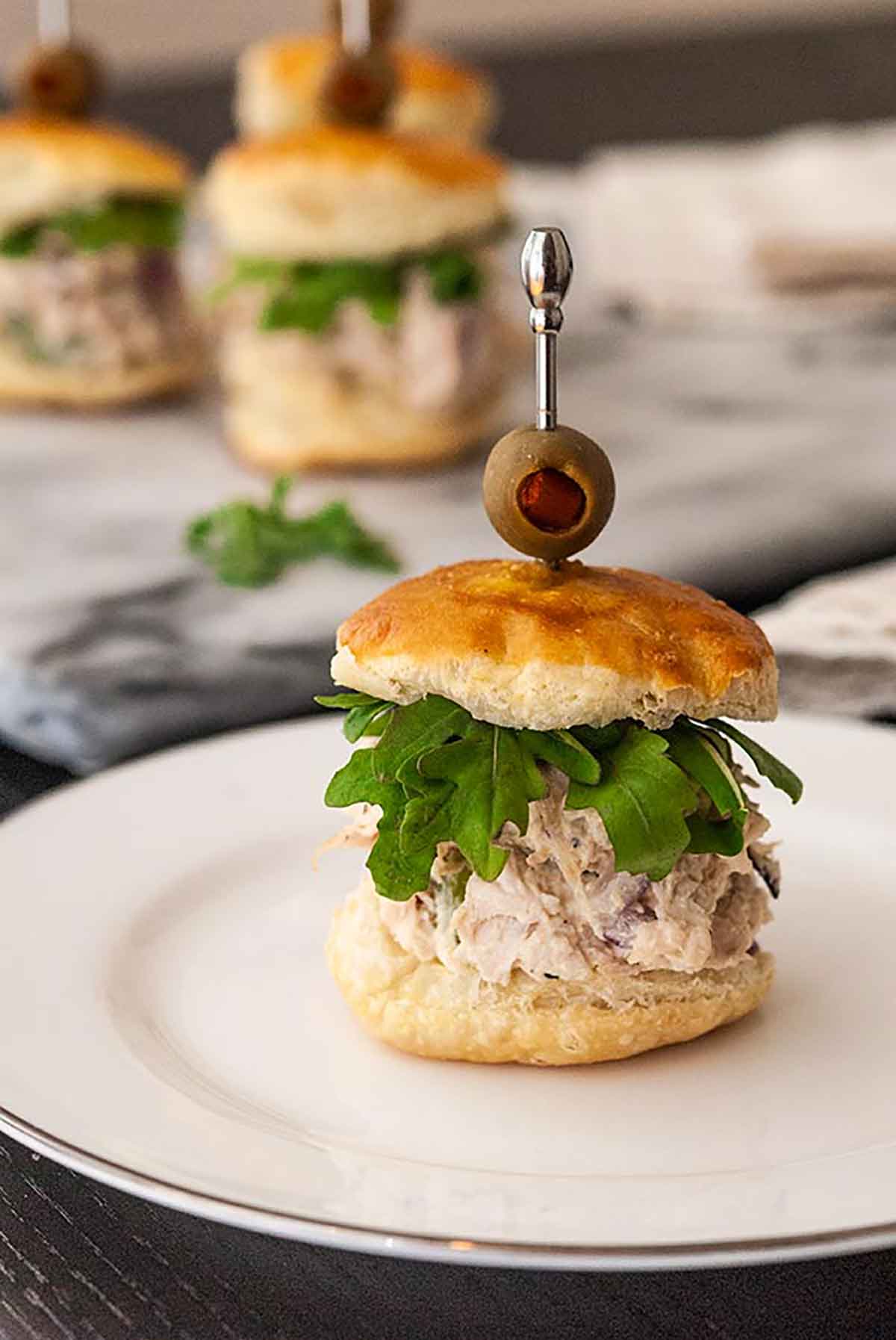 A chicken salad slider on a small plate with other sliders in the background.