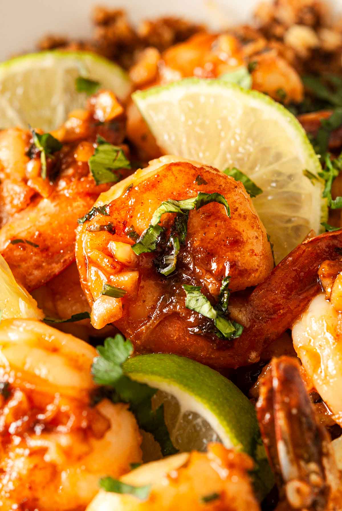 A honey lime shrimp in a bowl surrounded by lime slices and other cooked shrimp.