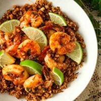 A bowl of lime shrimp atop coconut cauliflower rice on a lace tablecloth.