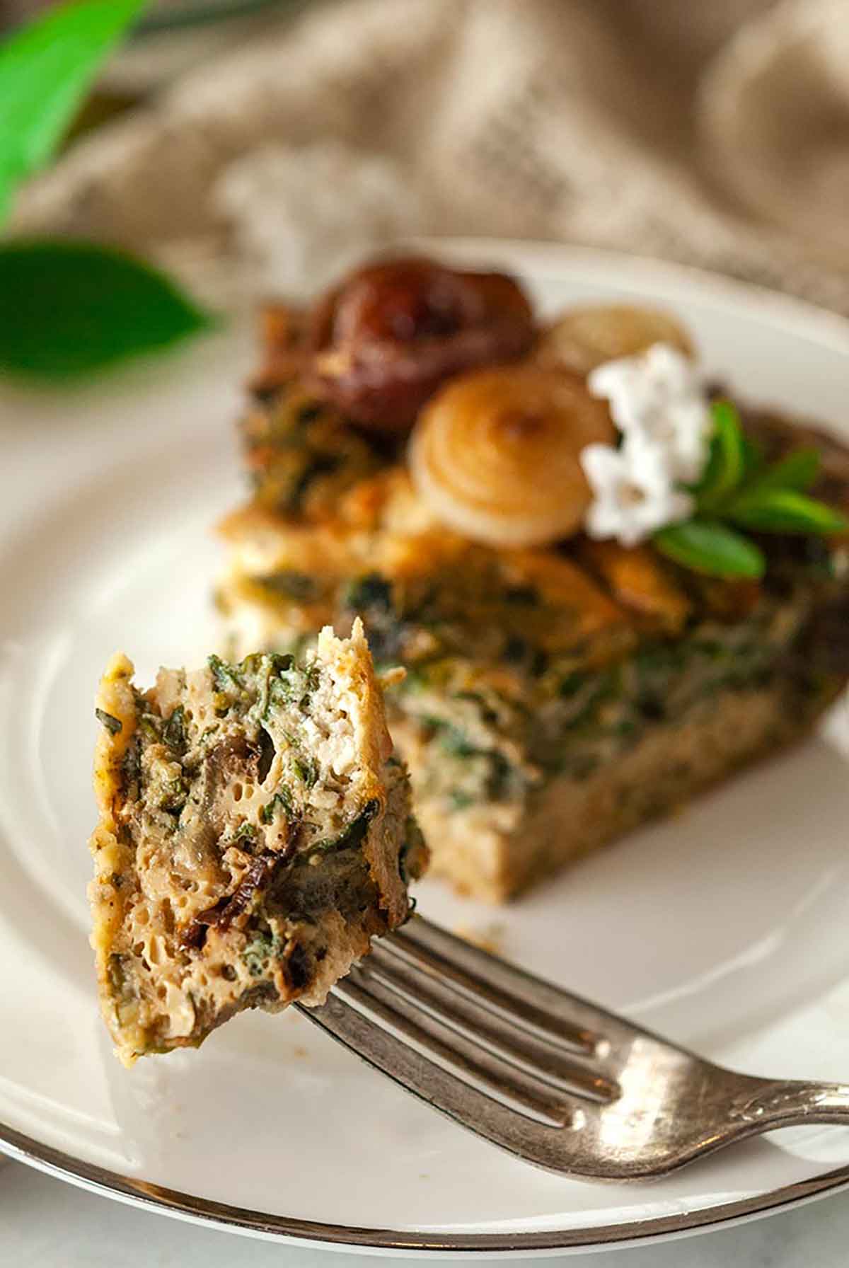 A piece of quiche on a fork with the slice in the background on a white plate.