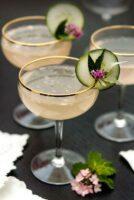 3 cocktails, garnished with a cucumber, leaf and small flowers with flowers at its base, as well as napkins.