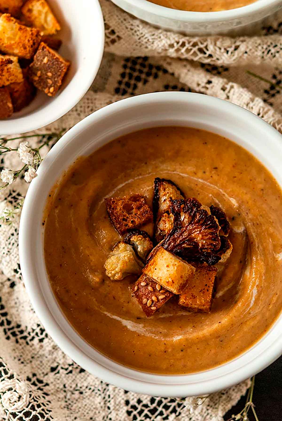 A bowl of cauliflower soup on a lace table cloth.