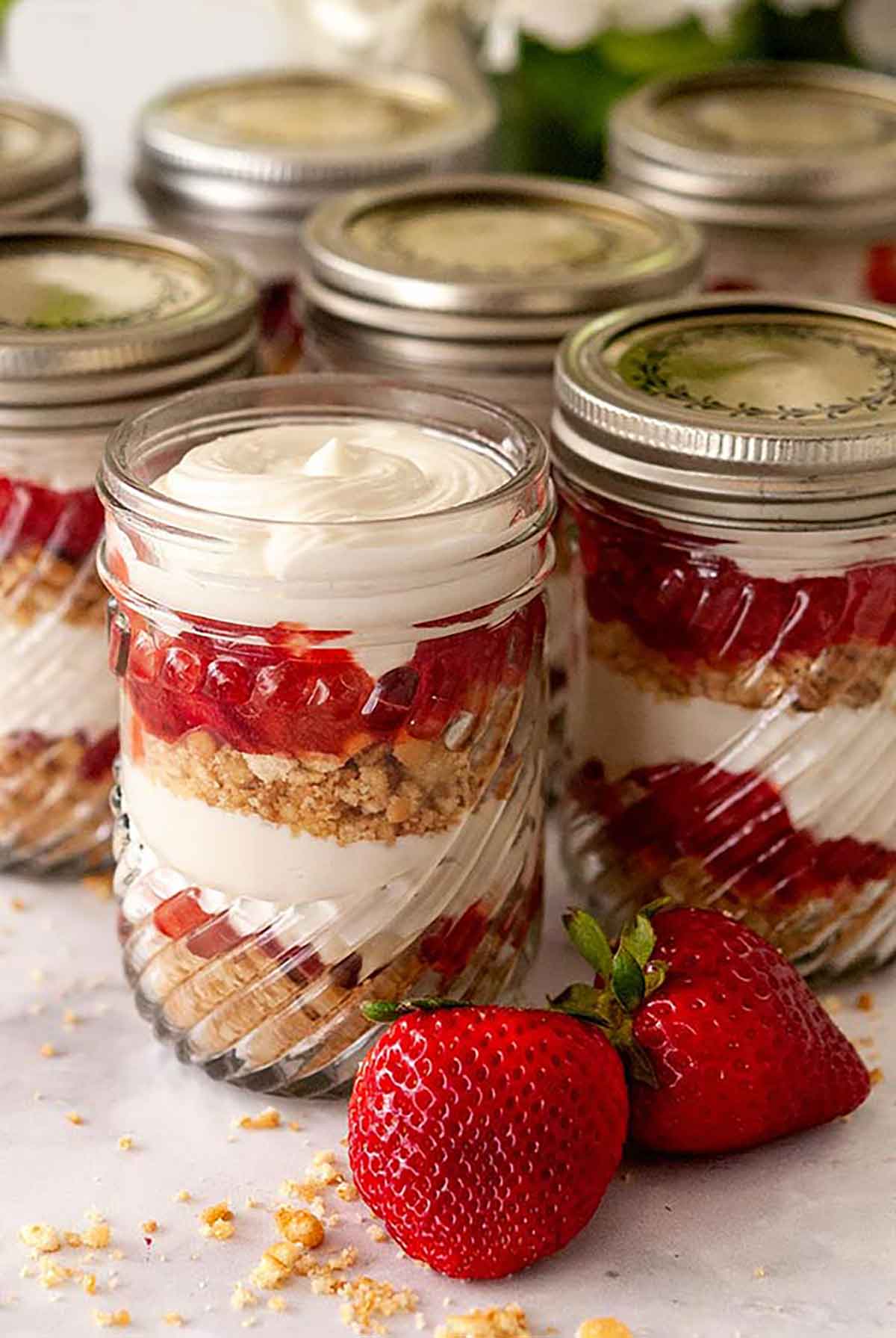 Strawberry rhubarb cups with vanilla cheesecake mouse on a marble table with a few strawberries beside them.