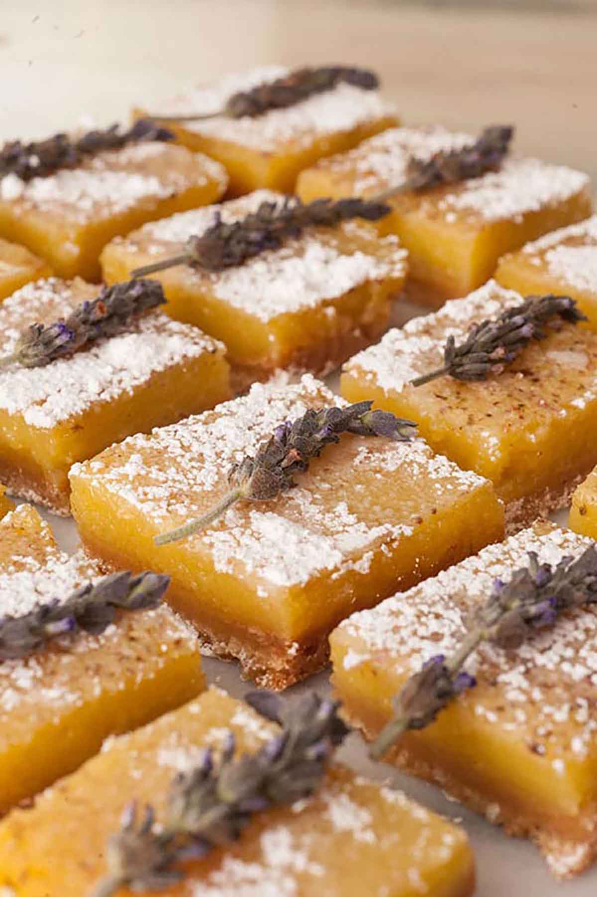 Lavender lemon bars, topped with fresh lavender on a white marble tray.