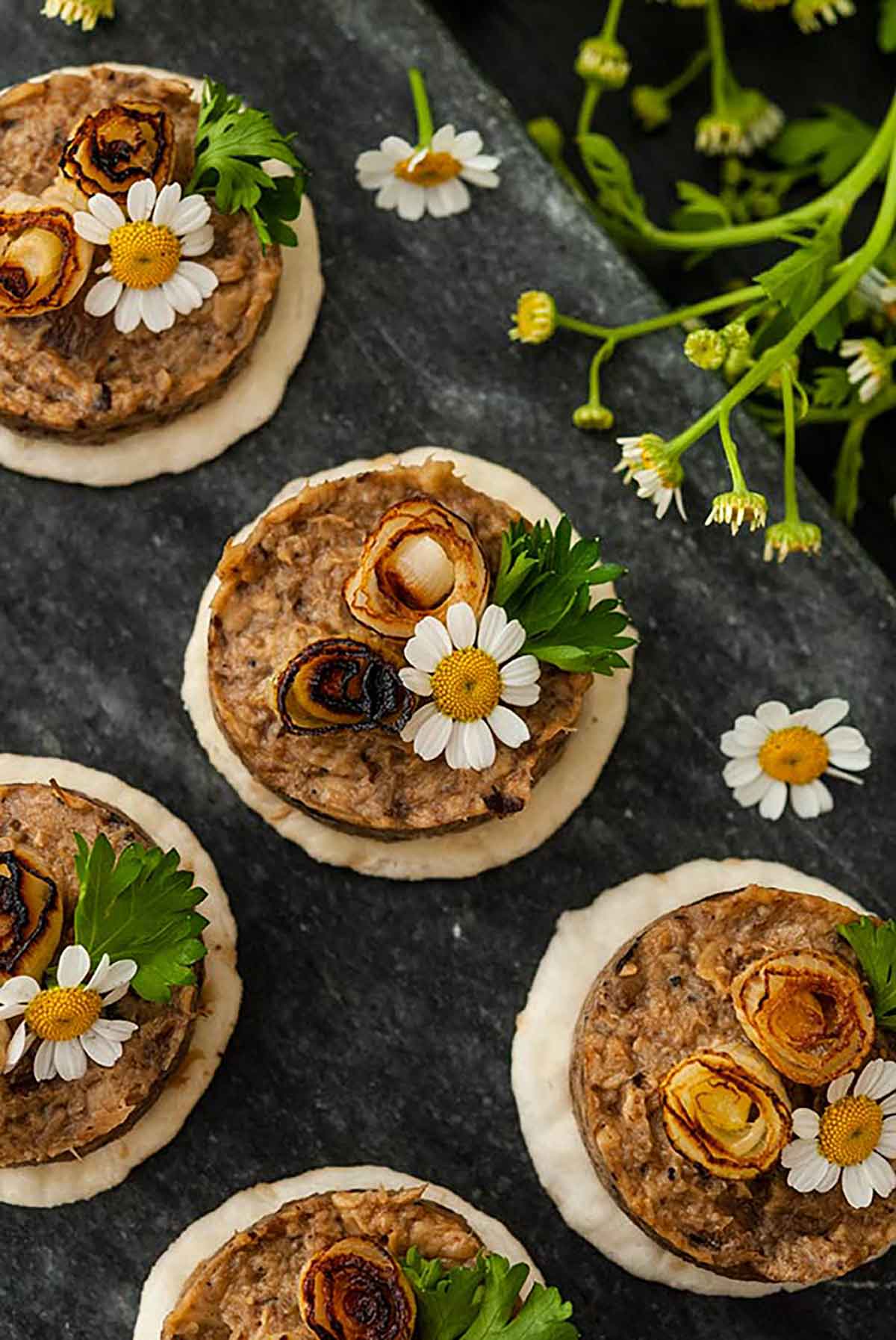 4 mushroom pâté canapés garnished with scallions and flowers on a marble slate.