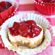 a cherry cheesecake in paper wrapping, topped with cherries on a gingham table cloth.