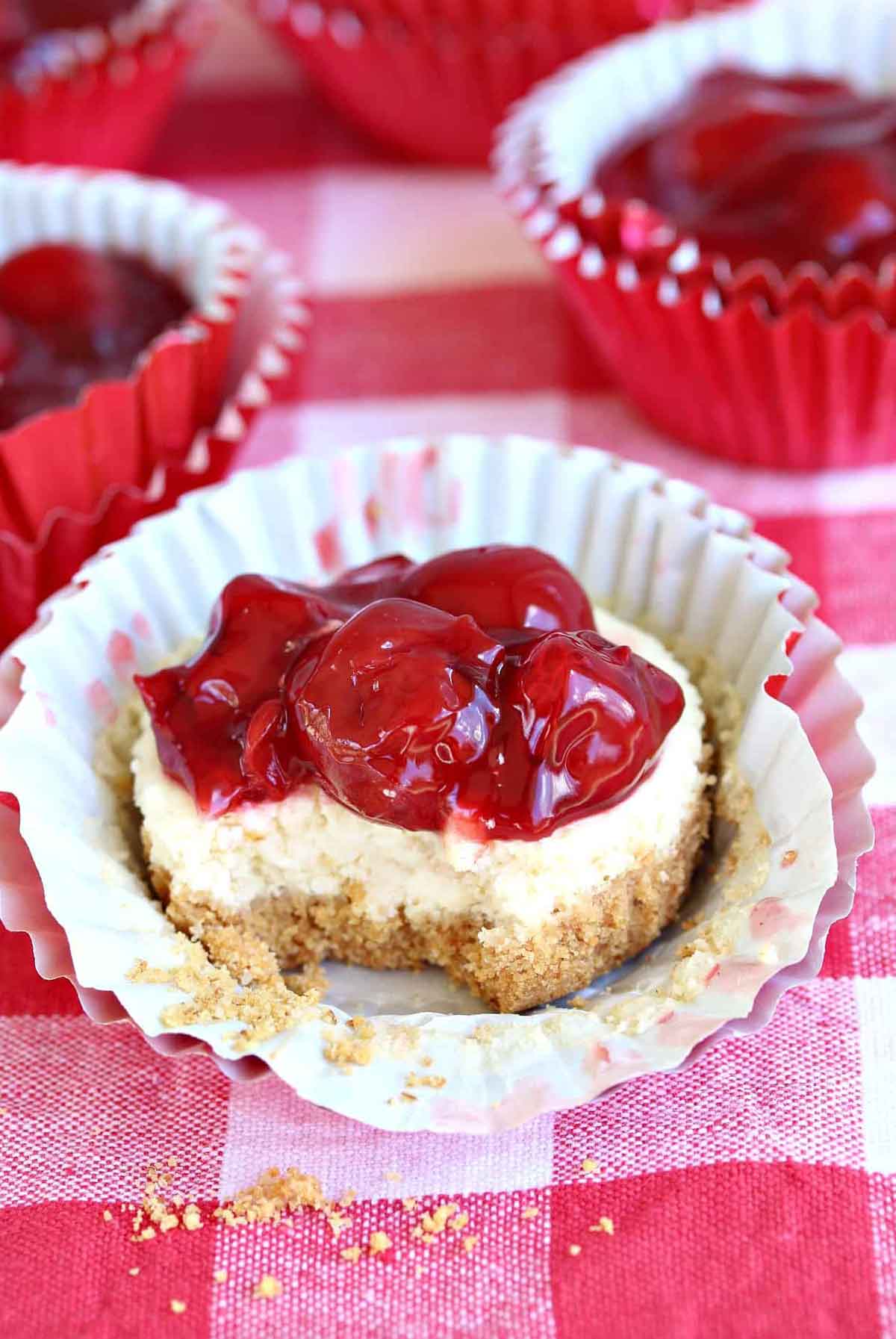 a cherry cheesecake in paper wrapping, topped with cherries on a gingham table cloth.