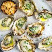 8 grilled oysters on a plate beside a grilled lemon slice.