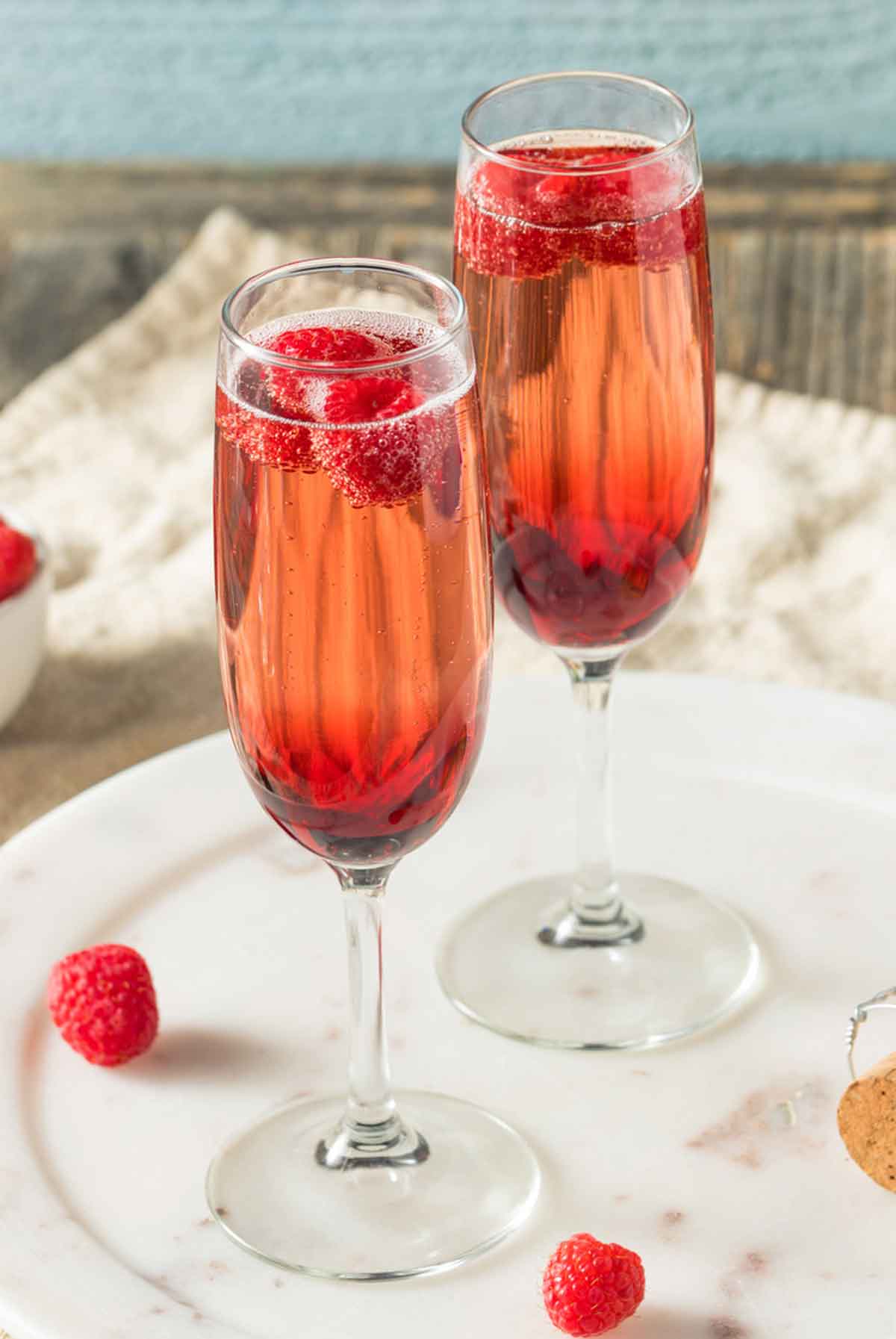 2 Kir Royale cocktails in champagne flutes on a table, garnished with raspberries.