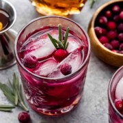 A maple cranberry smash cocktail on a table beside garnishes.