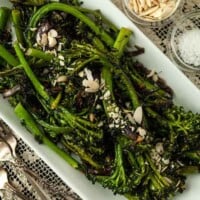 A plate of sautéed broccoli rabe on a lace tablecloth, beside 2 small bowls of garnish.