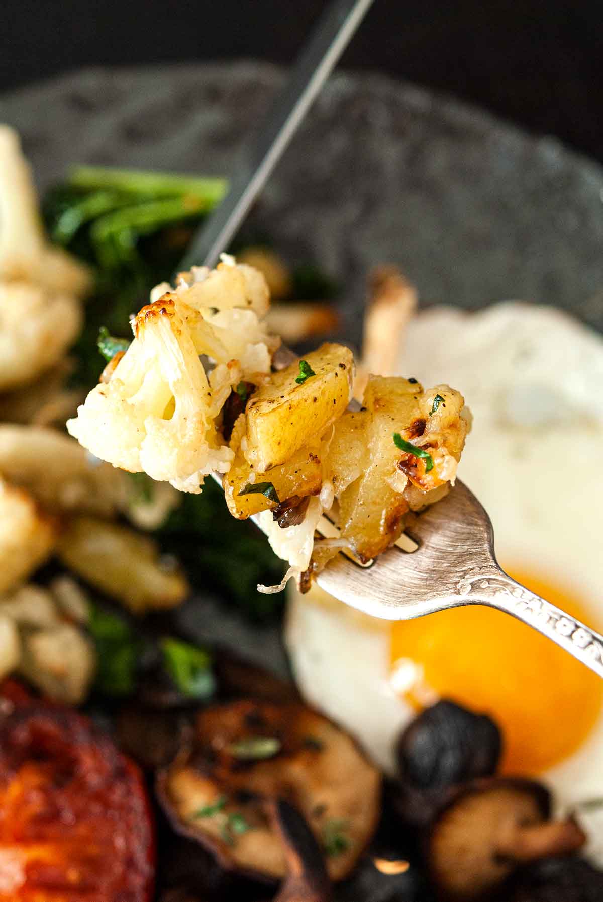 A fork full of potato-cauliflower hash, held above a plate of food.