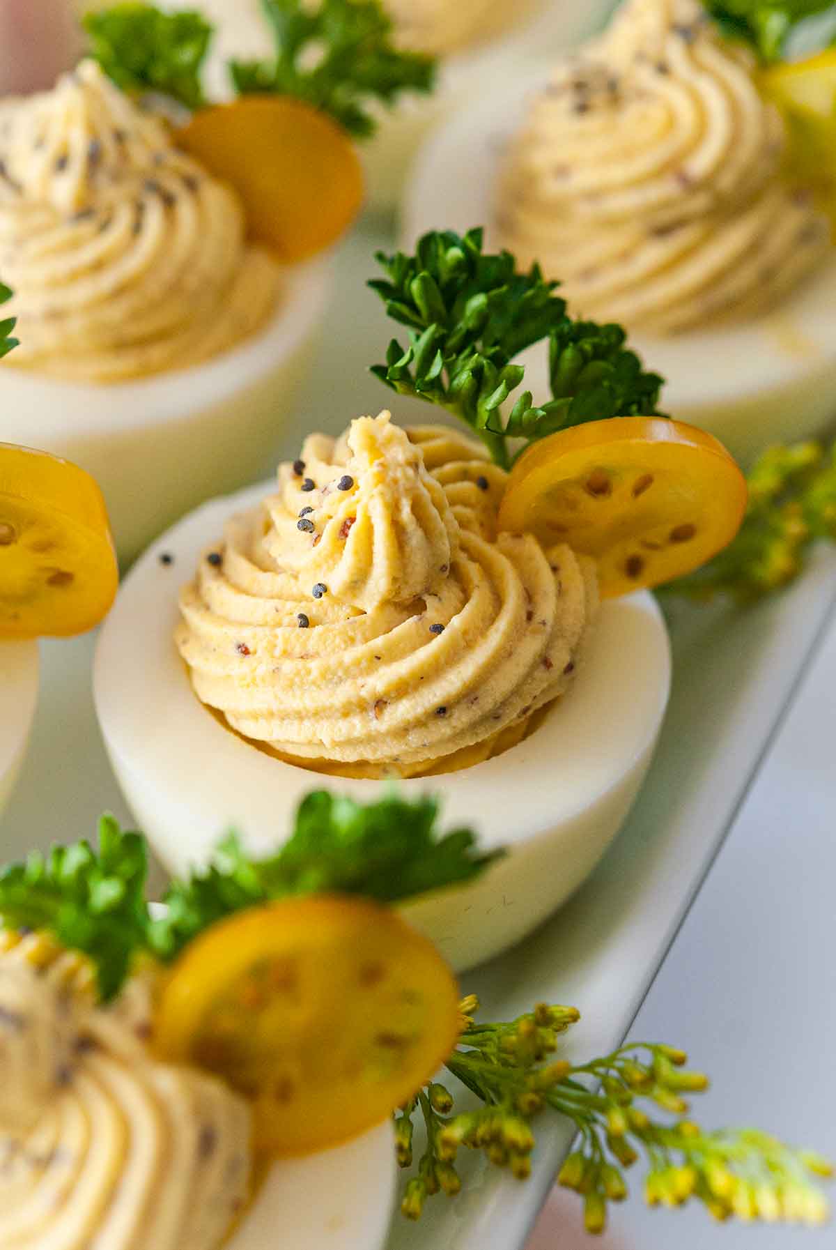 4 deviled eggs on a plate, garnished with tomatoes, parsley and poppyseeds.