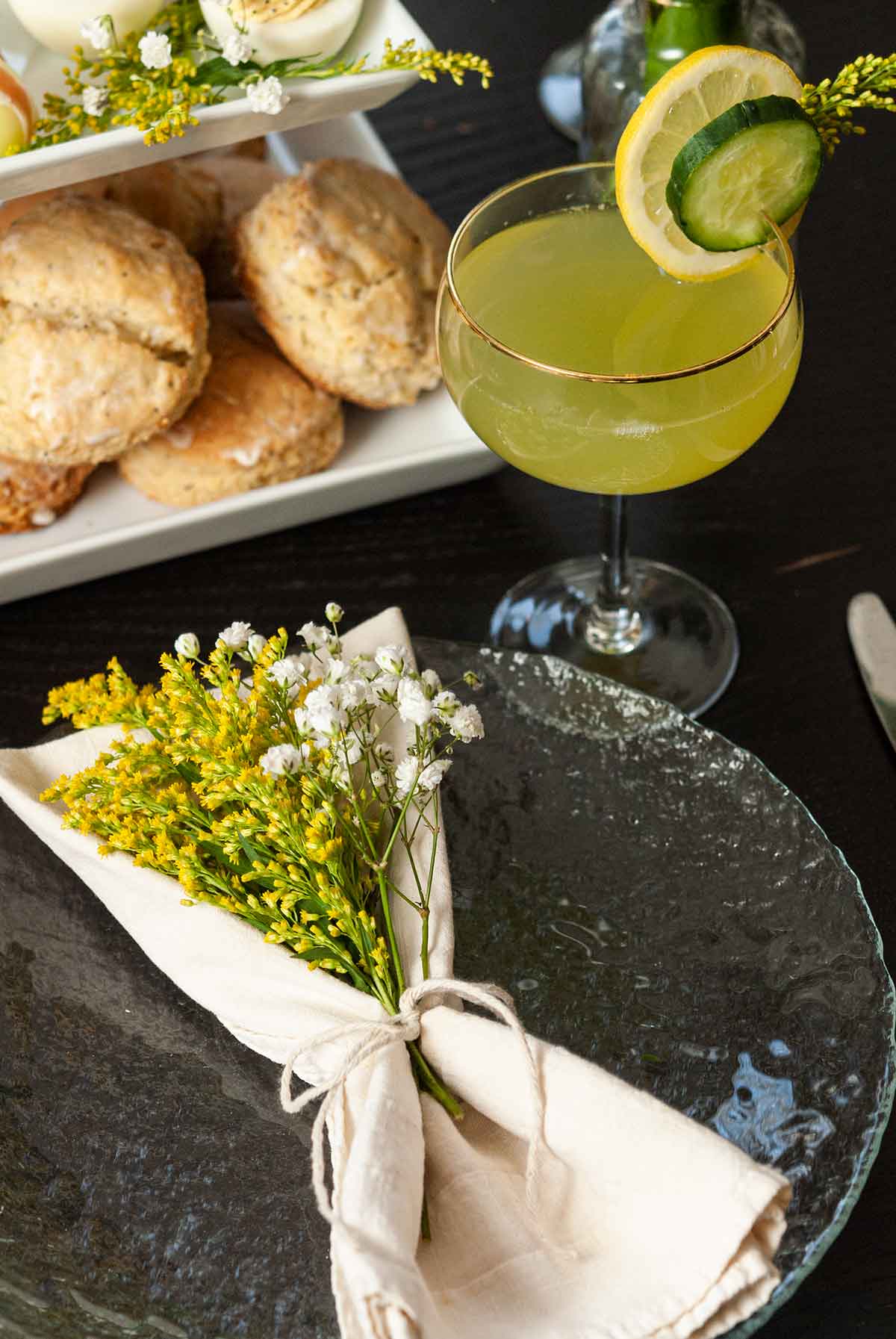 A place-setting of a napkin with flowers, a cocktail and a tier of sones on a table.