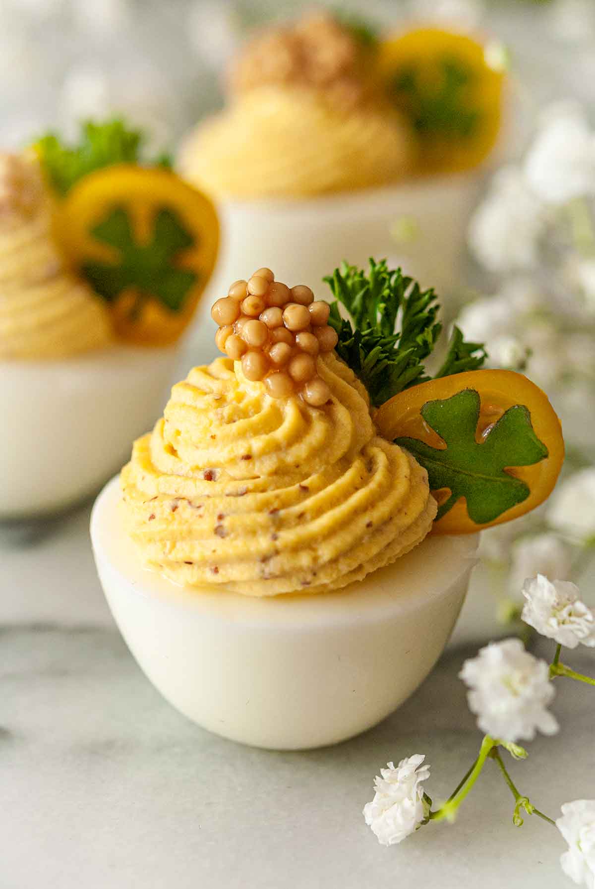 3 deviled eggs, garnished with tomato, clover, parsley and a dollop of mustard caviar on marble.