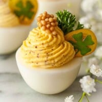 A deviled egg, garnished with tomato, clover, parsley and a dollop of mustard caviar on marble.