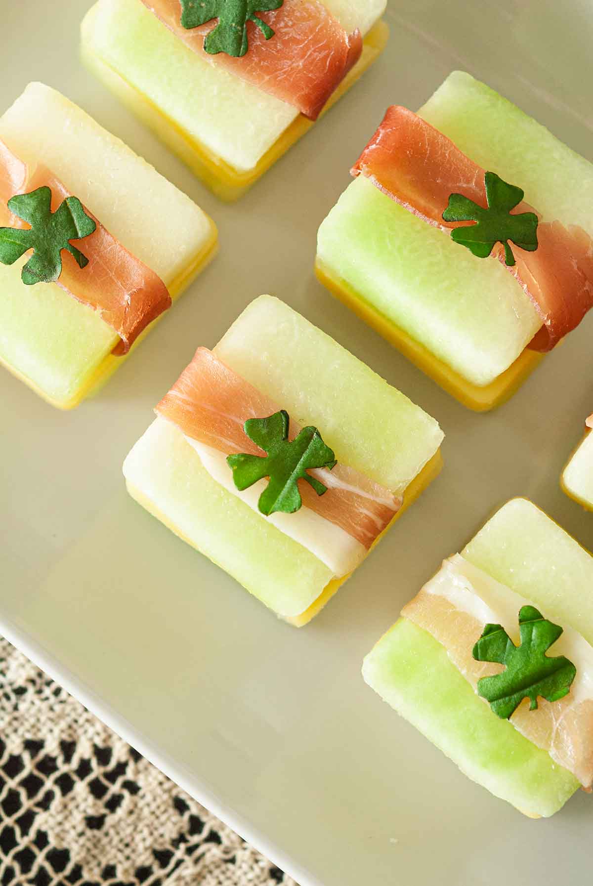 5 St. Patrick's Day melon appetizers with clovers on top, on a white plate.