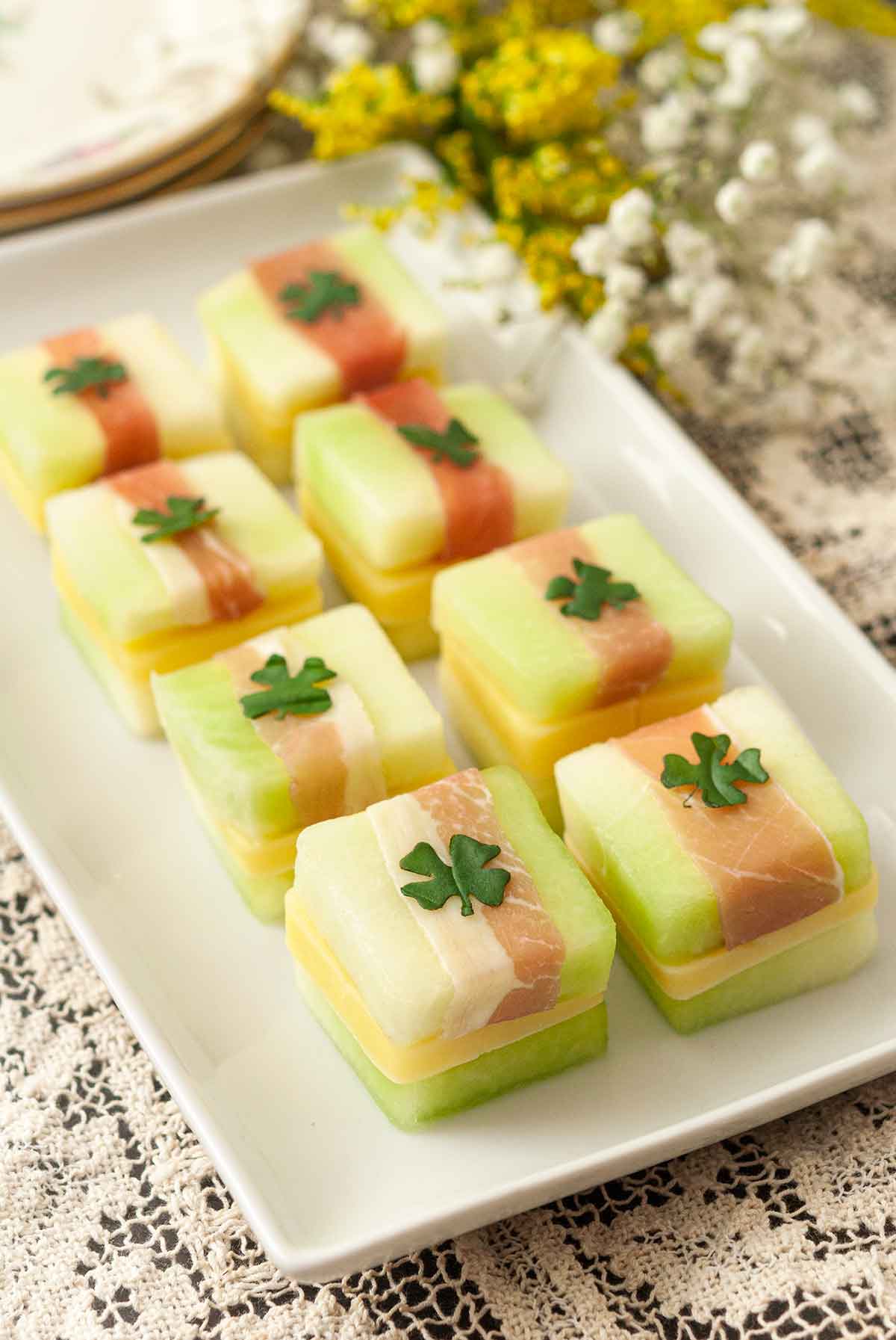 8 St. Patrick's Day melon appetizers with clovers on top, on a white plate, on a lace table cloth..