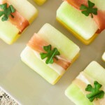 4 St. Patrick's Day melon appetizers with clovers on top, on a white plate.