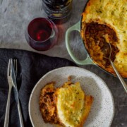 A rustic plate of cottage pie on a plate beside a full pie on a table.