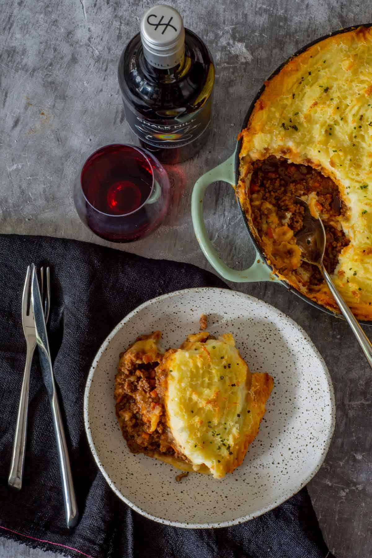 A rustic plate of cottage pie on a plate beside a full pie on a table.