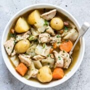 A bowl of chicken stew with potatoes and carrots on a table.