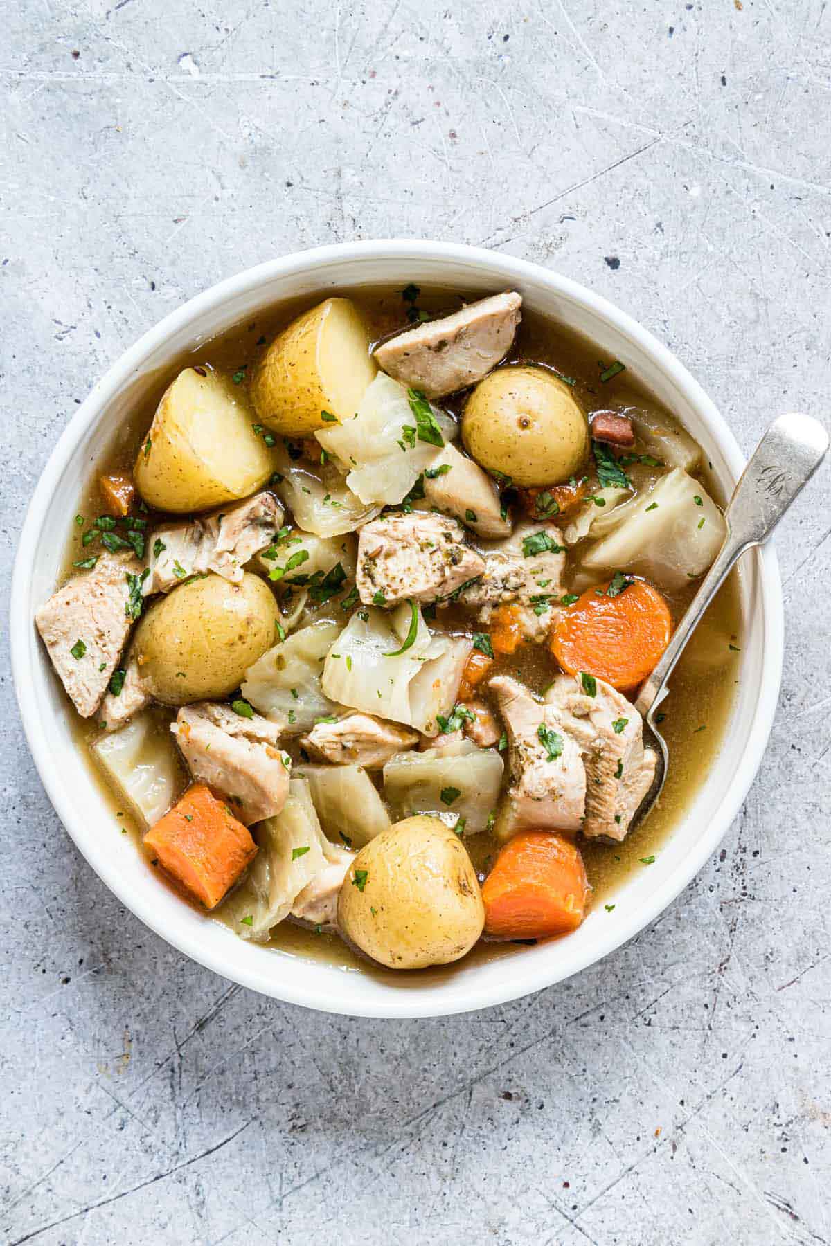 A bowl of chicken stew with potatoes and carrots on a table.