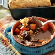 A bowl of beef stew next to a pan of bread.