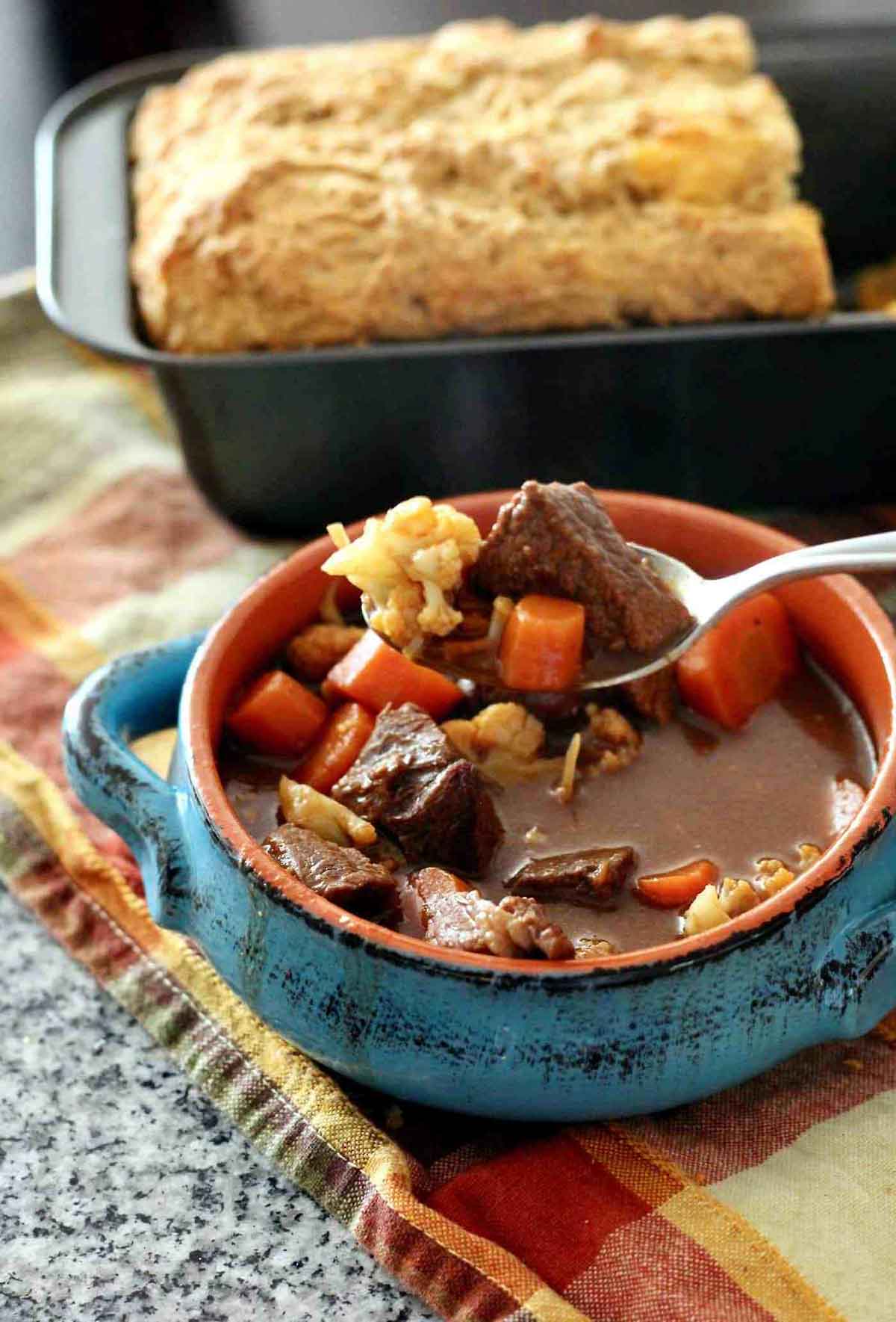 A bowl of beef stew next to a pan of bread.