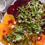 Sliced beets on a plate with arugula and pepitas.