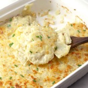 A baking dish full of potatoes au gratin, with a spoon lifting some up.