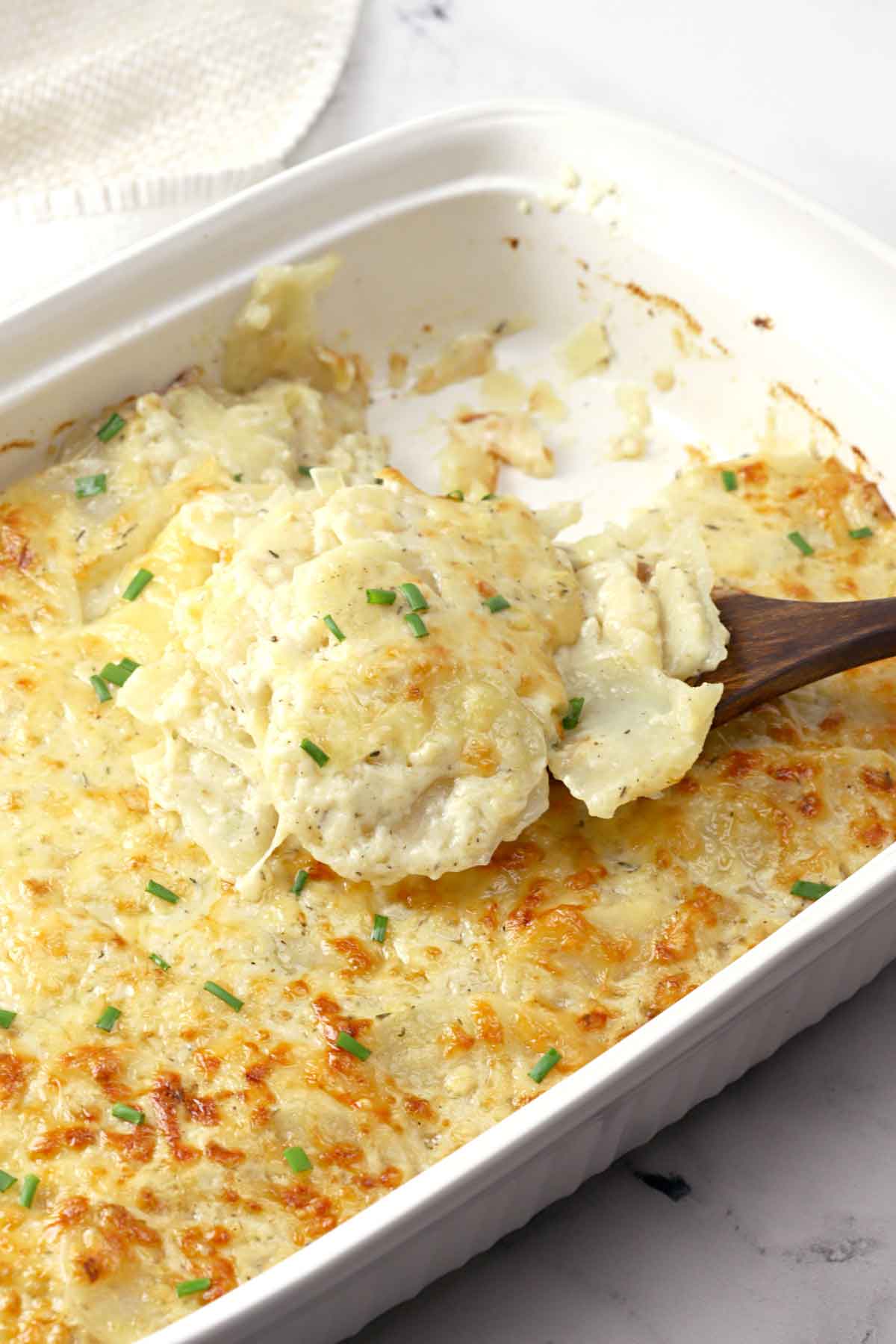 A baking dish full of potatoes au gratin, with a spoon lifting some up.