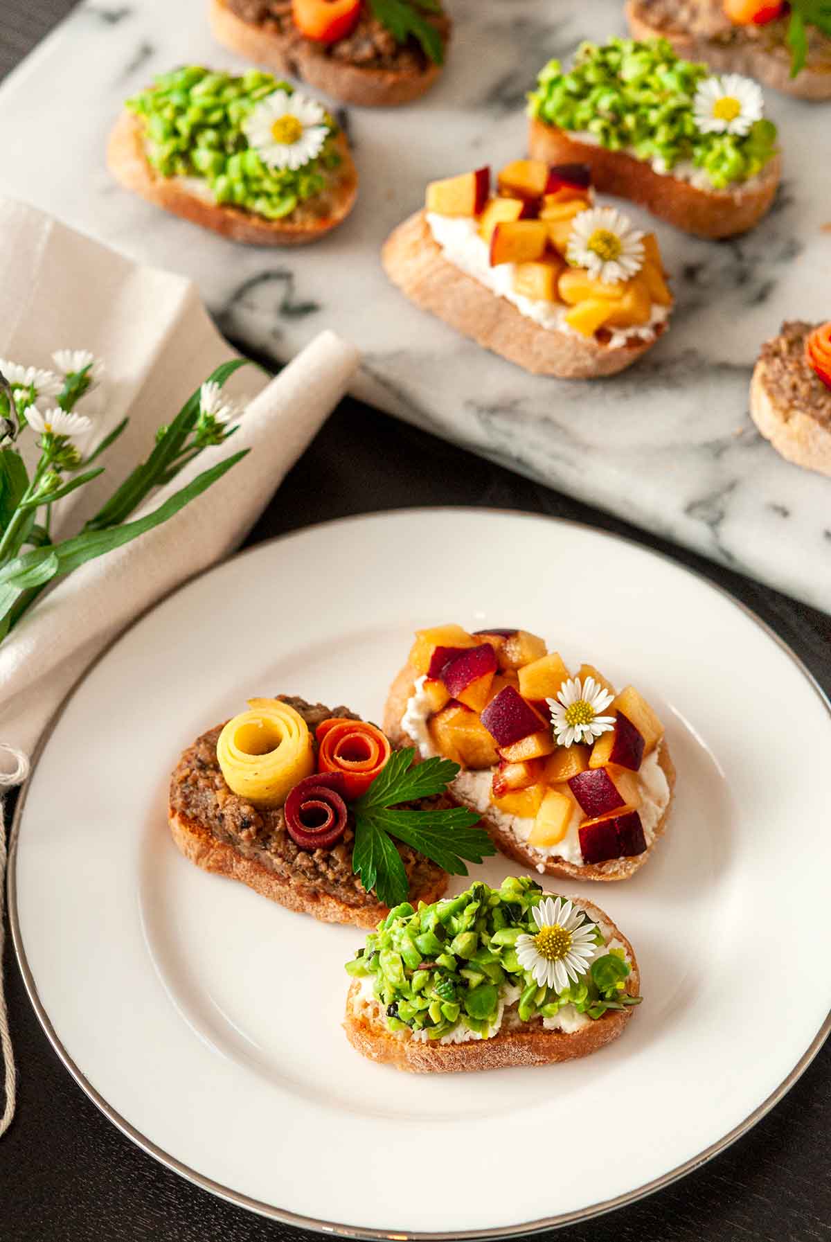 3 crostini on a small plate beside a marble appetizer slate, and napkin.