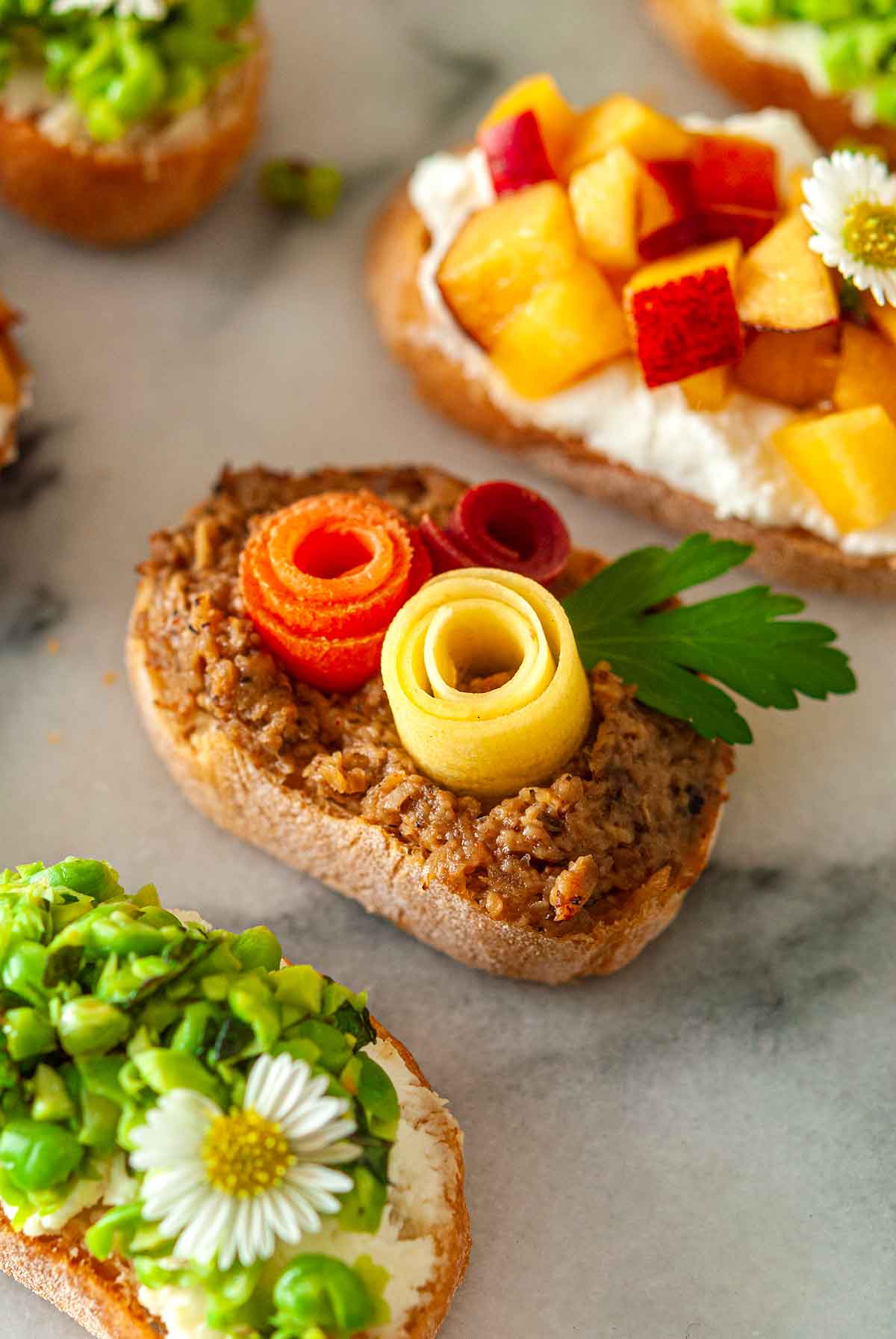 5 brightly colored crostini on a plate, with a carrot rose crostini in the center.