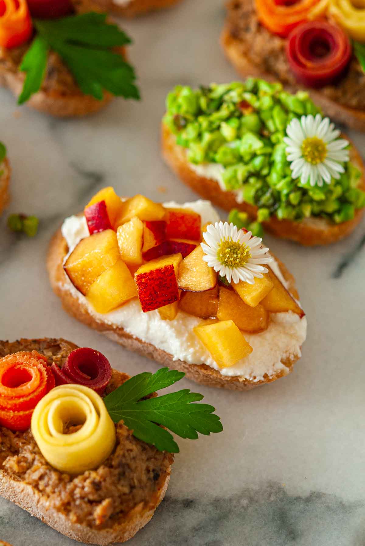 5 brightly colored crostini on a plate, with a peach crostini in the center.